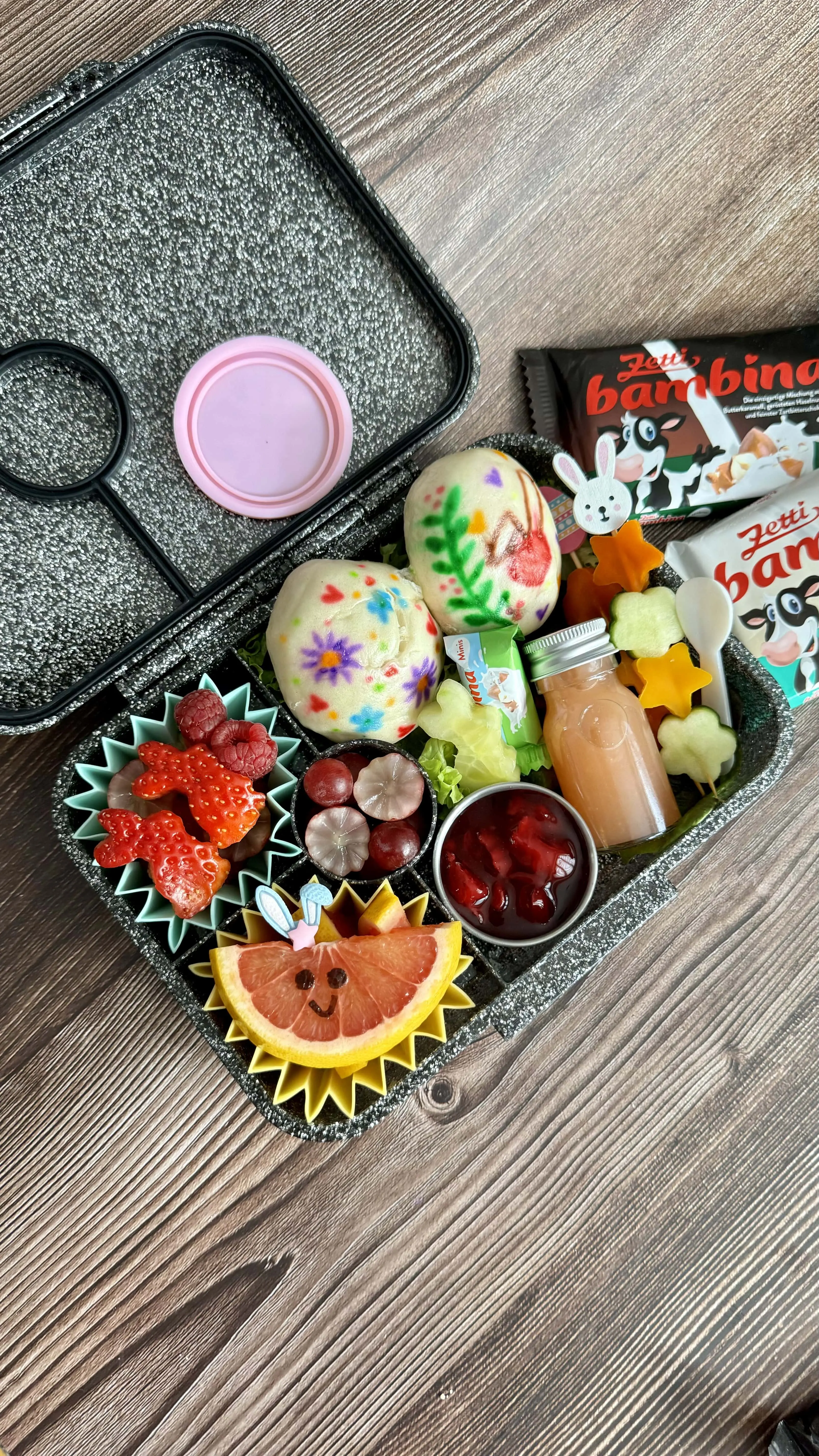 mit Früchten und bemalten Bao Buns befüllte Brotdose. Daneben liegen Zetti Bambina Tafeln