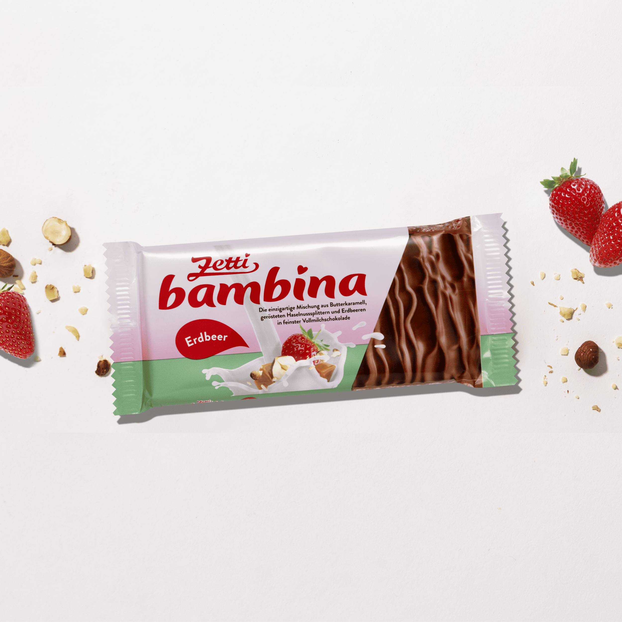 Eine Tafel Zetti Bambina Erdbeer eingebettet neben Haselnüssenund Erdbeeren.