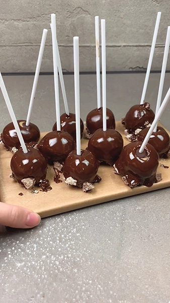 Cakepops mit dunkler Schokolade überzogen, stehen auf einem Holzbrett 