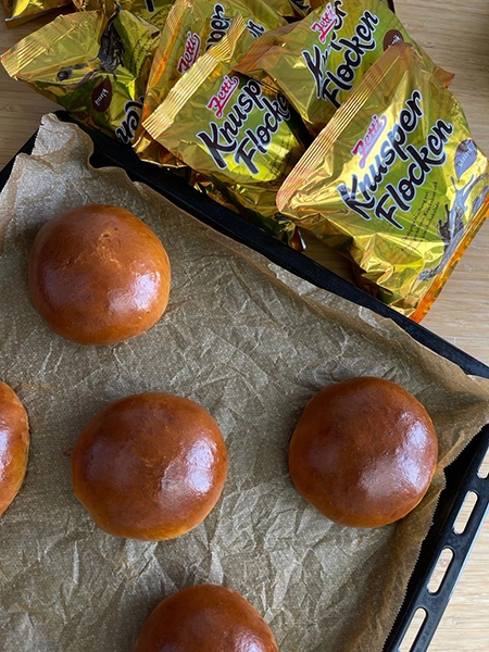 Brioche Brötchen auf einem Backblech. Daneben liegen mehrere Knusperflocken Tüten